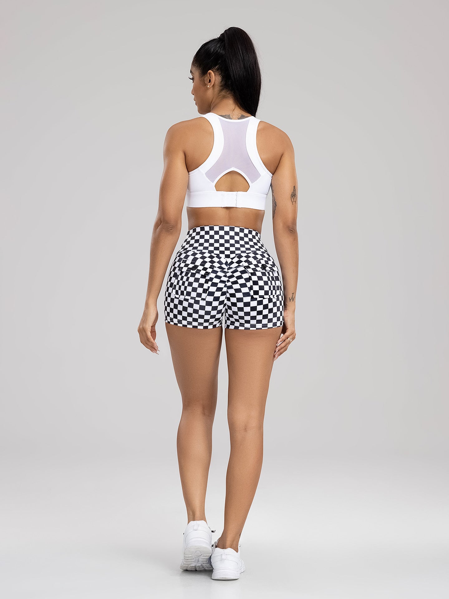 Woman wearing a white sports bra and black and white checkered shorts on a gray background